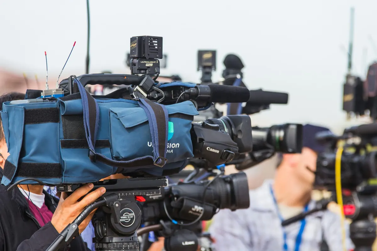 Een rij broadcastcamera's van tv-ploegen naast elkaar bij een persmoment, als symbool voor traditionele media-aandacht.